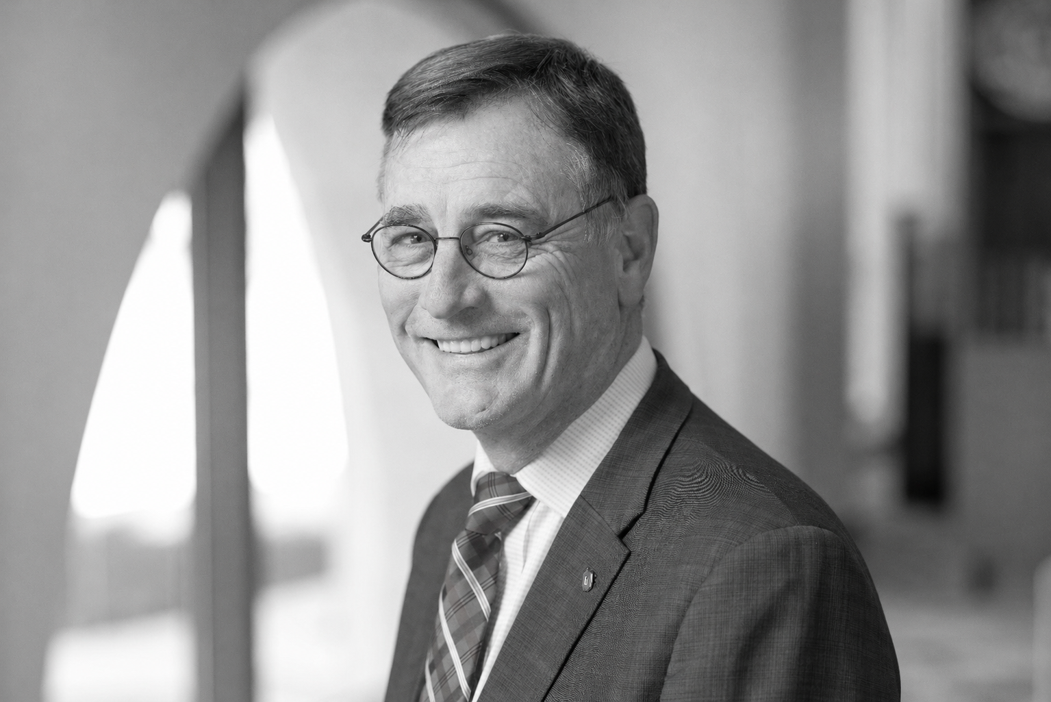 Smiling man in a suit and striped tie, wearing round glasses, looking at the camera in a professional setting