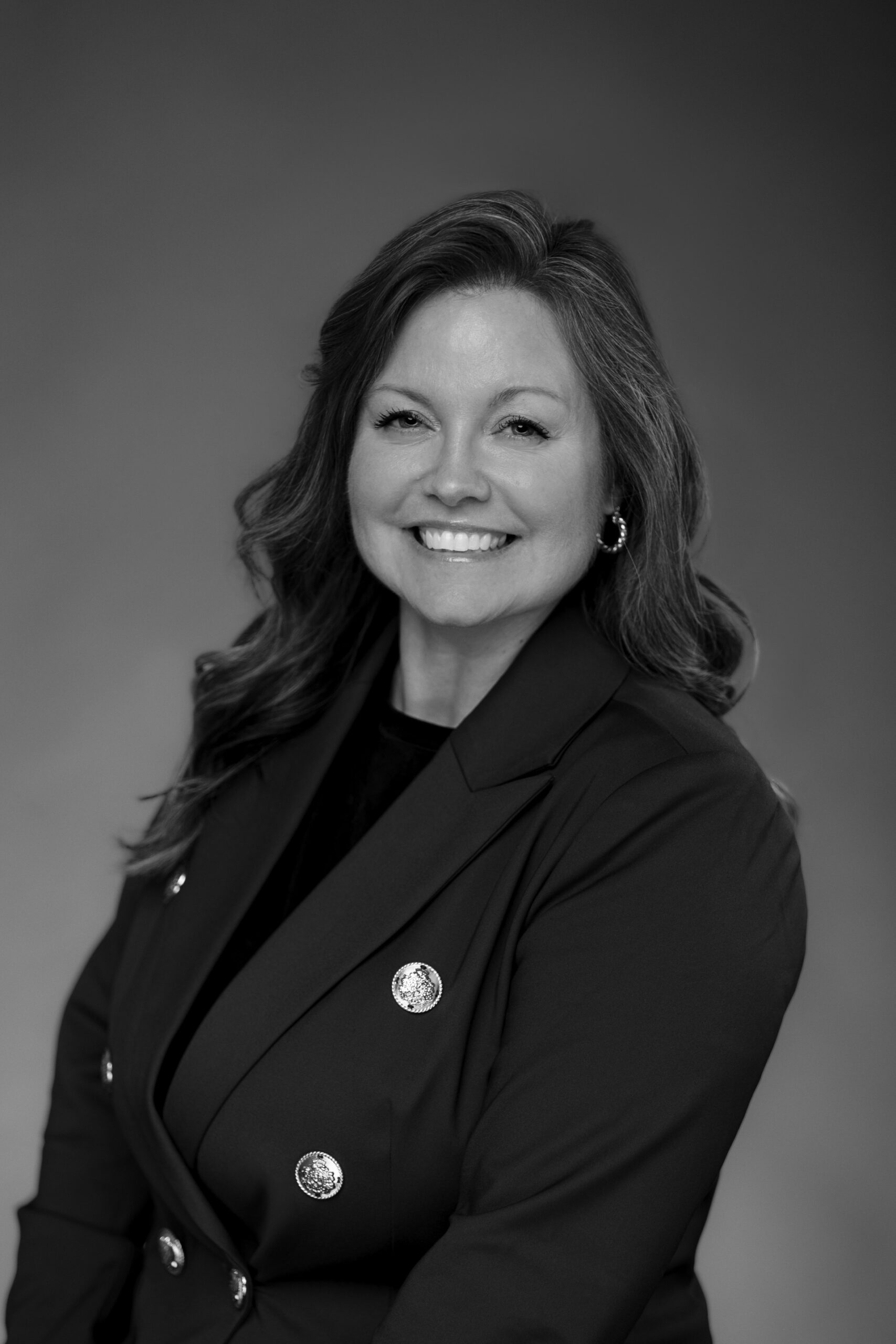 Smiling woman in a dark blazer with decorative metal buttons in a grayscale professional portrait.