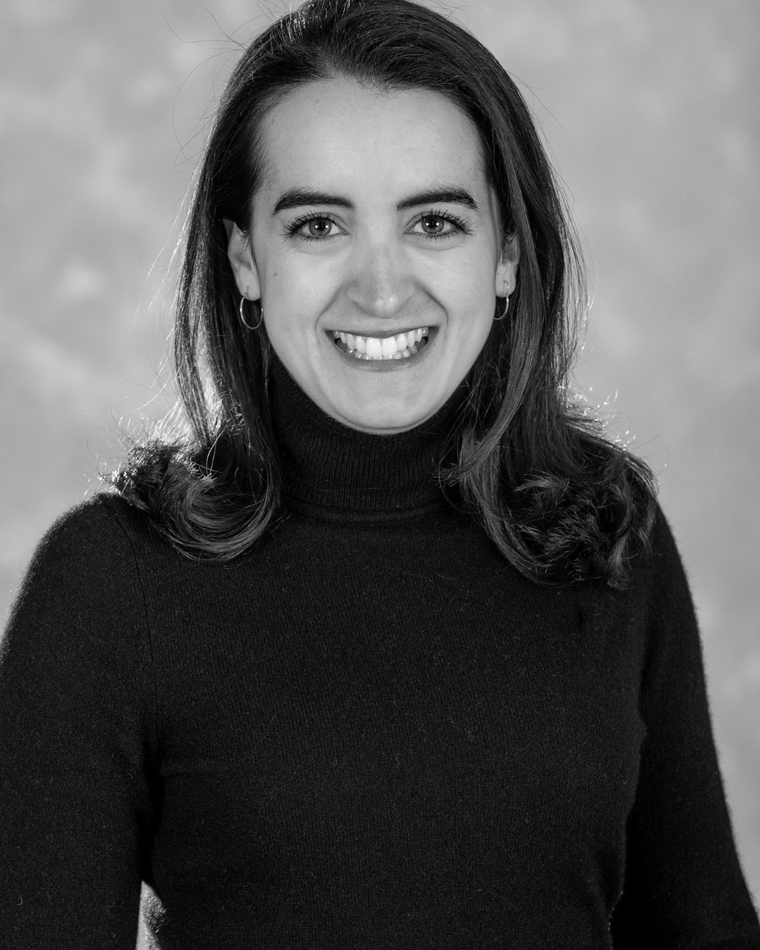 Head-and-shoulders portrait of a smiling woman with dark hair wearing a black turtleneck sweater, looking at the camera.
